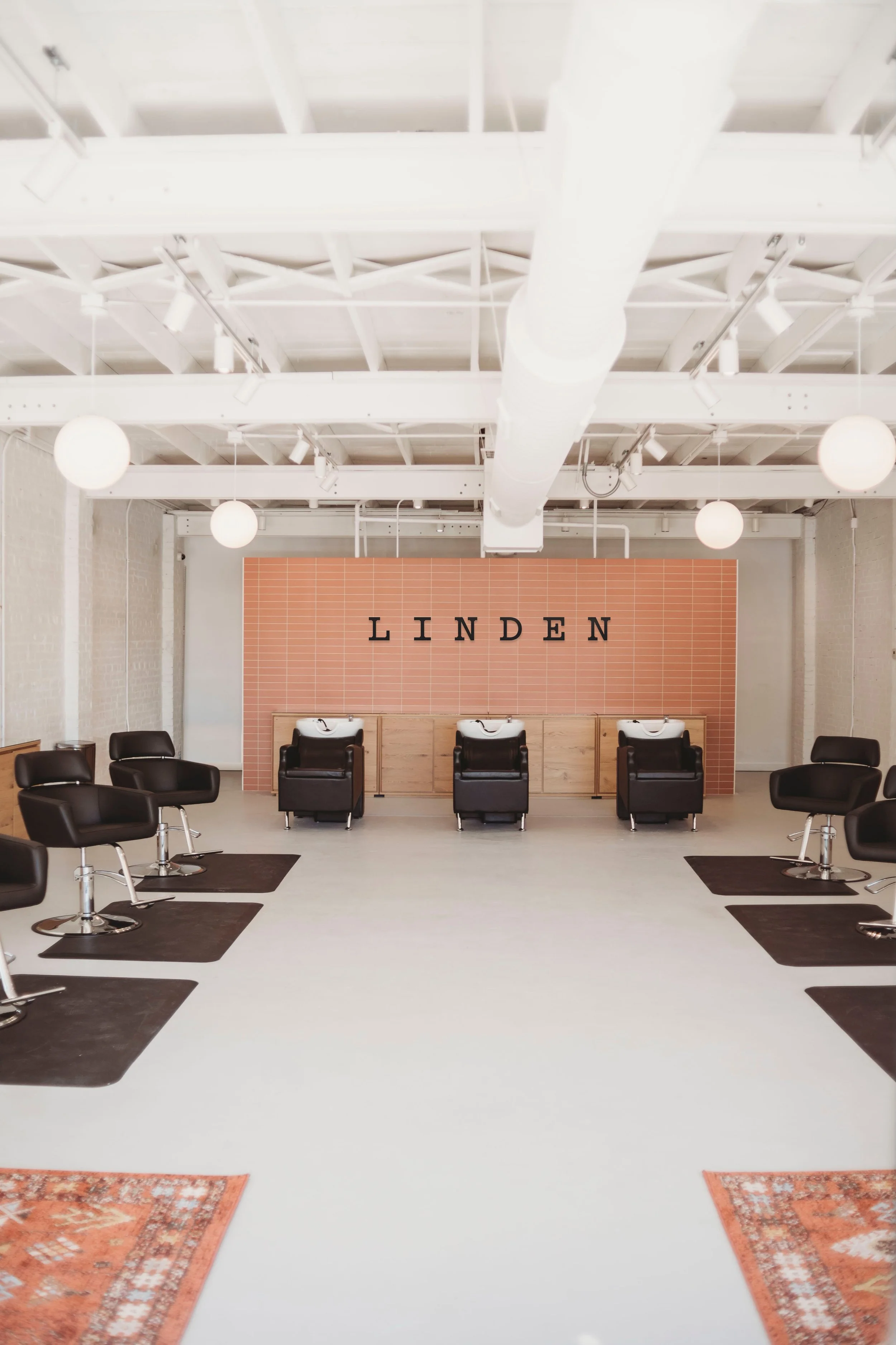 A salon is shown with large acrylic letters that say "Linden" and has black salon chairs and pink tile.